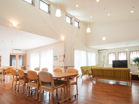 白い壁でフローリングの床の空間は広々としており、天井は高く開放感がある。机や椅子が置かれ、窓際にはテレビとソファがある。