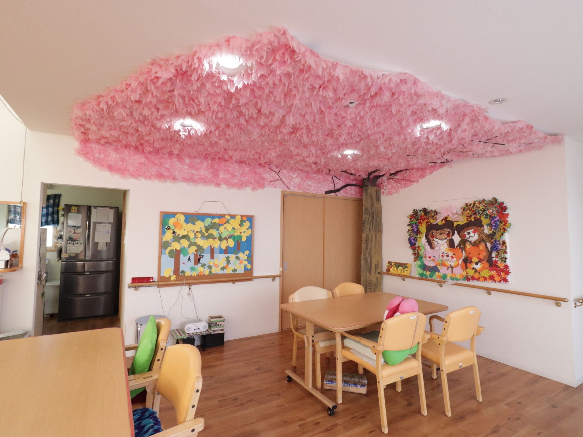 満開の桜の木の飾りが施された食堂である。桜の花びらがついた天井の下には白木のテーブルと黄色の背もたれがついた椅子が設置されている。
