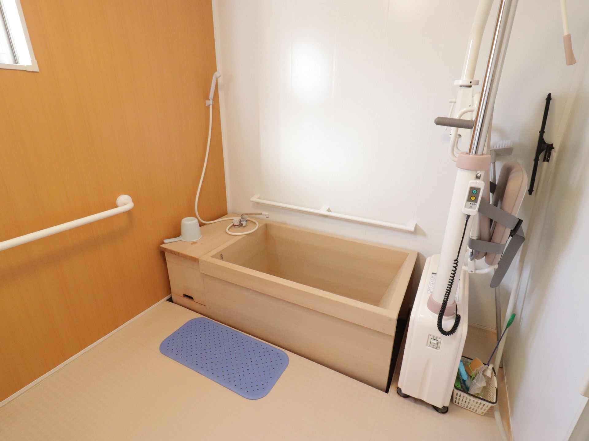ひのきの浴槽が使われた浴室である。入浴を介助するリフトが設置されている。浴槽と色を合わせた壁が使われている。