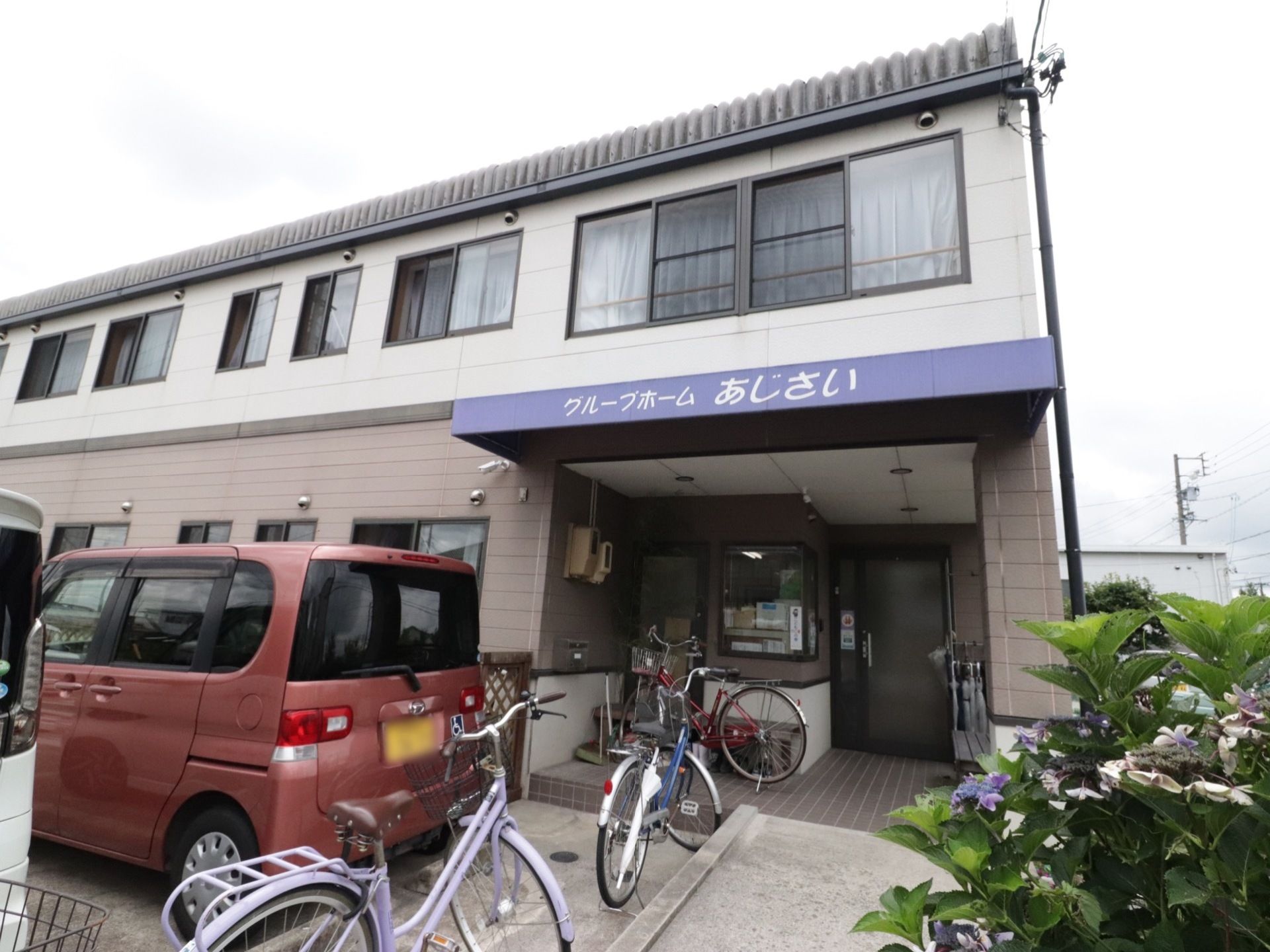 施設はベージュ色が基調となった２階建ての建物である。建物の前には駐車場や、自転車を駐輪することができるスペースがある。