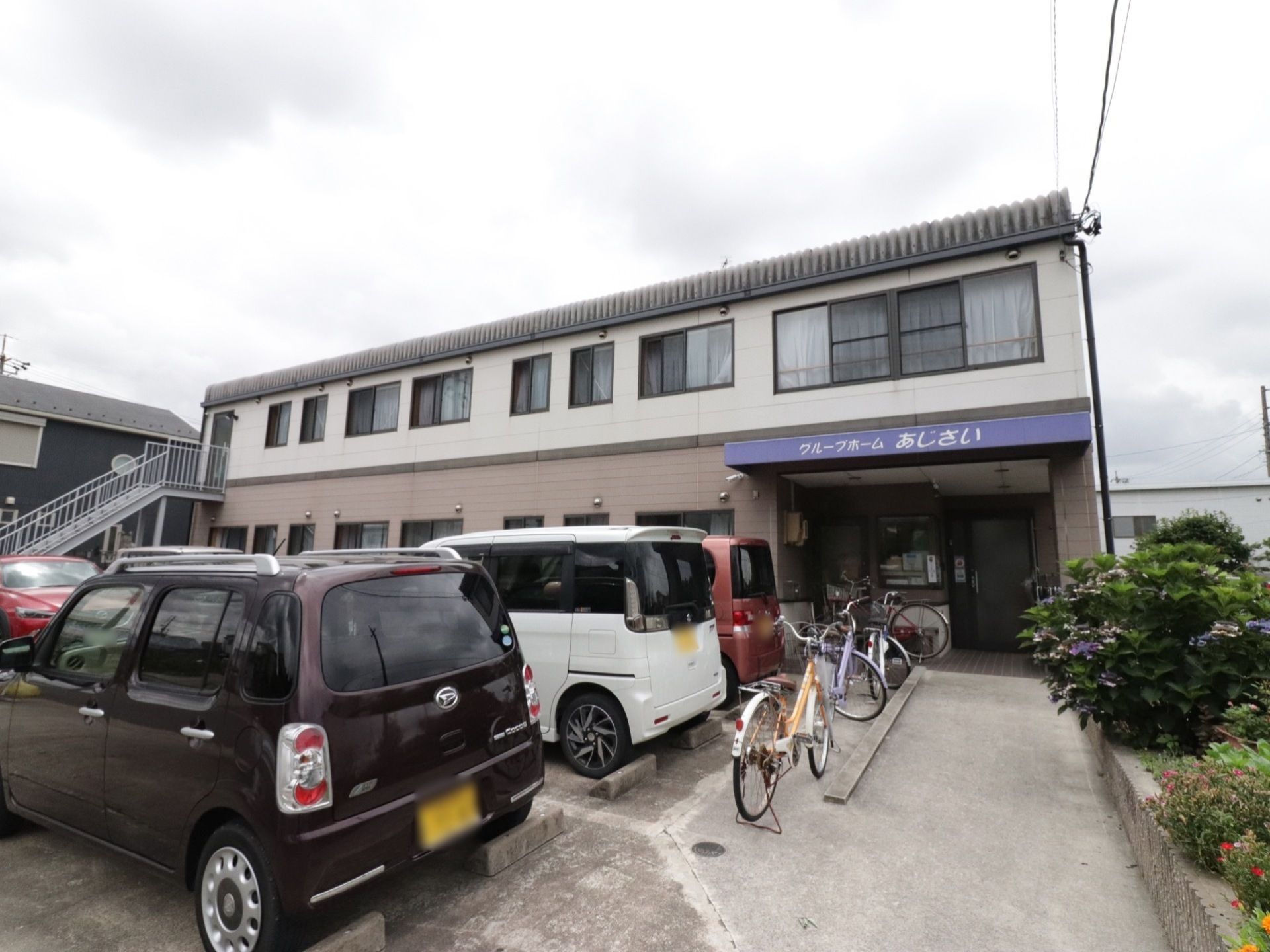 広い駐車スペースがあり、外階段が設置された２階建ての施設外観