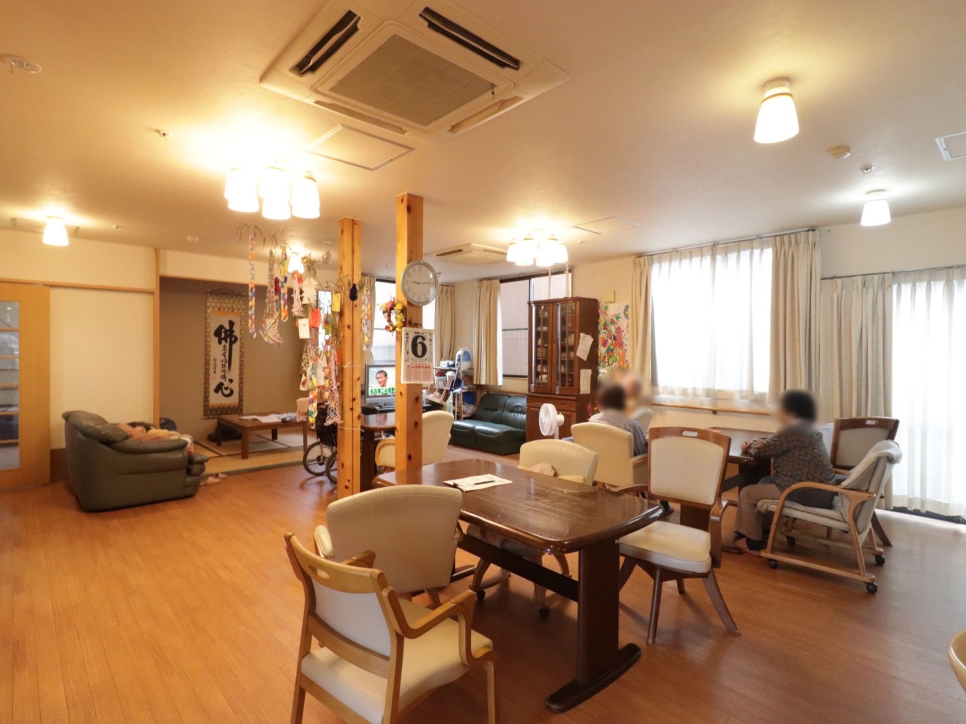 テーブル席やソファーに座った入居者様がテレビをご覧になっている。テレビの左側には畳が設置されている。