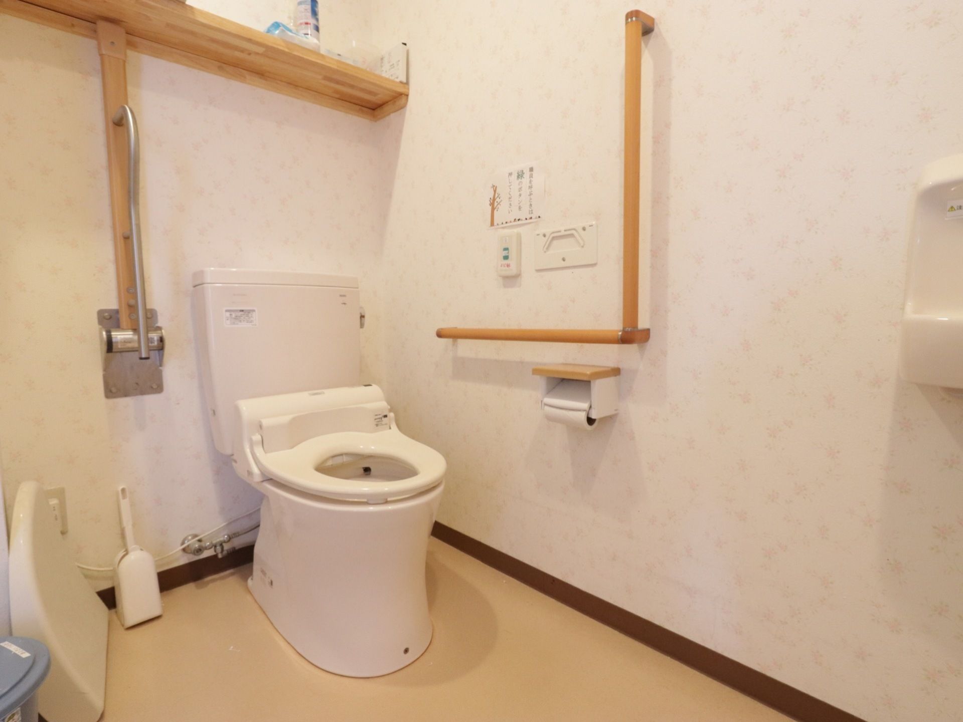 共有トイレには、跳ね上げ式やL型手すり、洗面台が完備されている。壁には、棚や呼び出しボタンが設置されている。