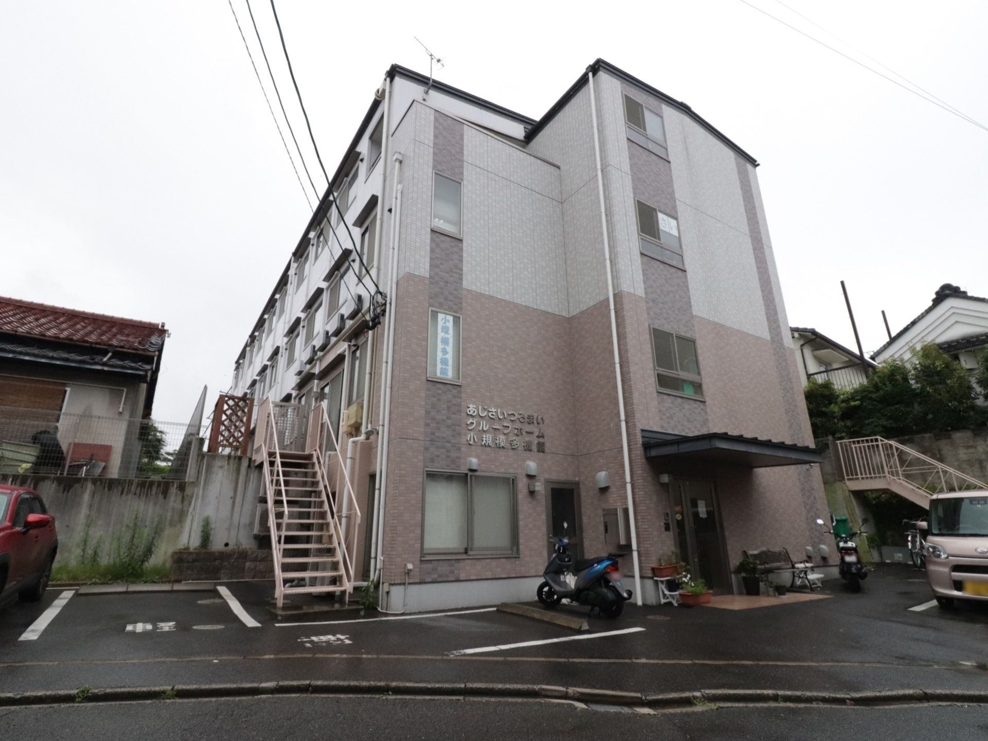 住宅地に建てられた小豆色の４階建ての施設。駐車場も設けており、ご家族の方が面会に来られた際にご利用いただける。