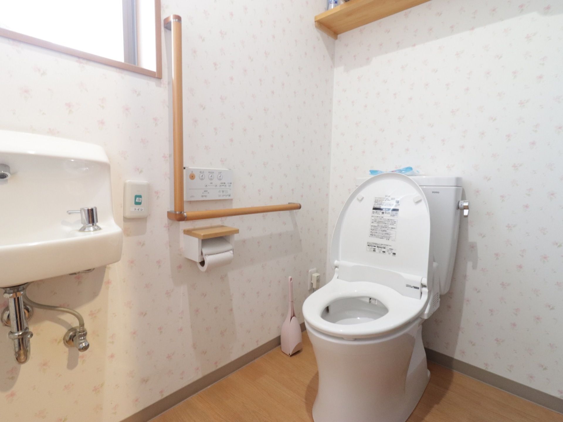 ポップな壁紙が印象的な、明るいトイレである。温水洗浄便座を完備。壁にはL型の手すりを備えつけている。