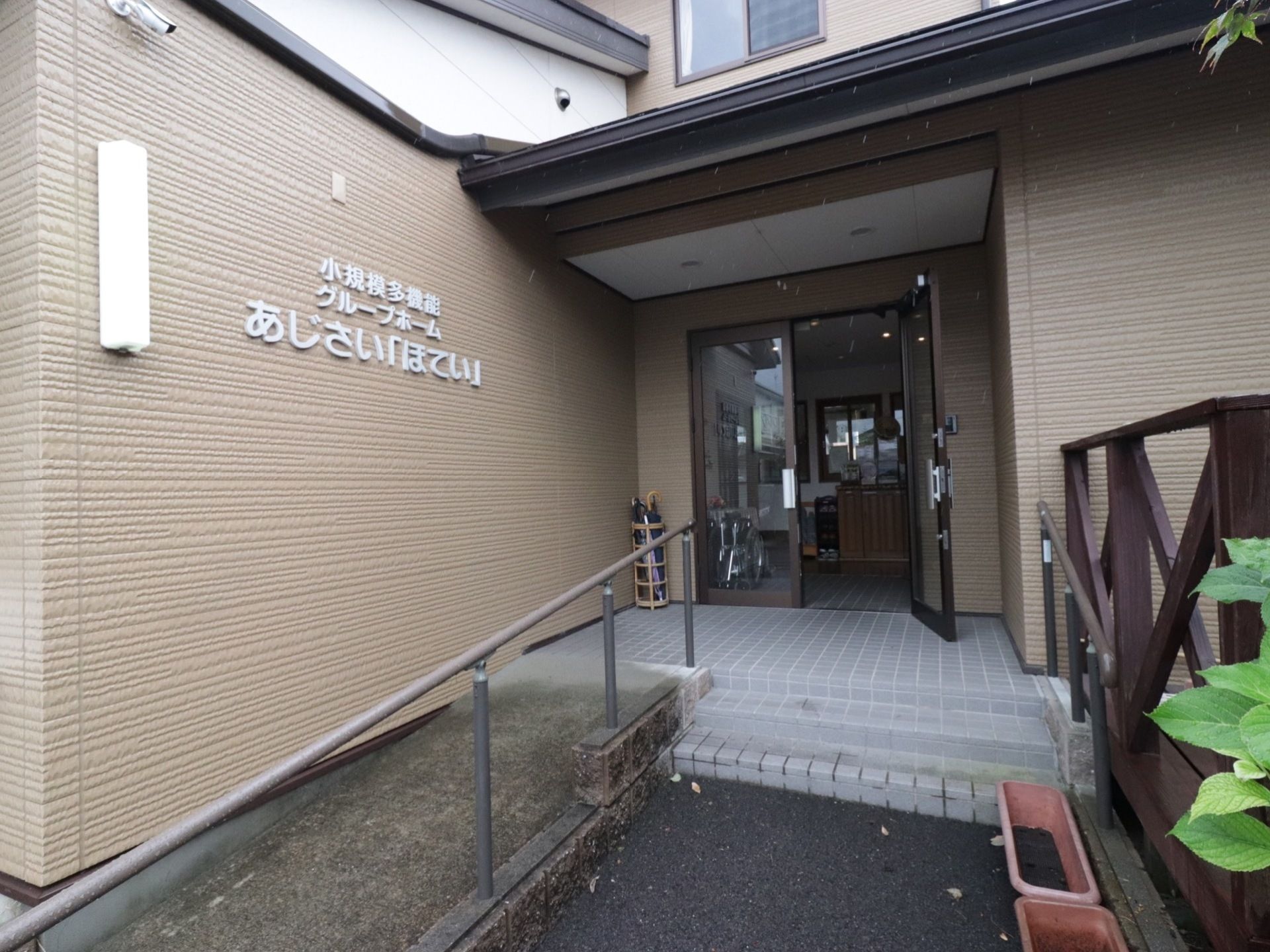 落ち着いた色調で統一されたエントランスである。玄関前には階段、手すりがついたスロープが完備されている。