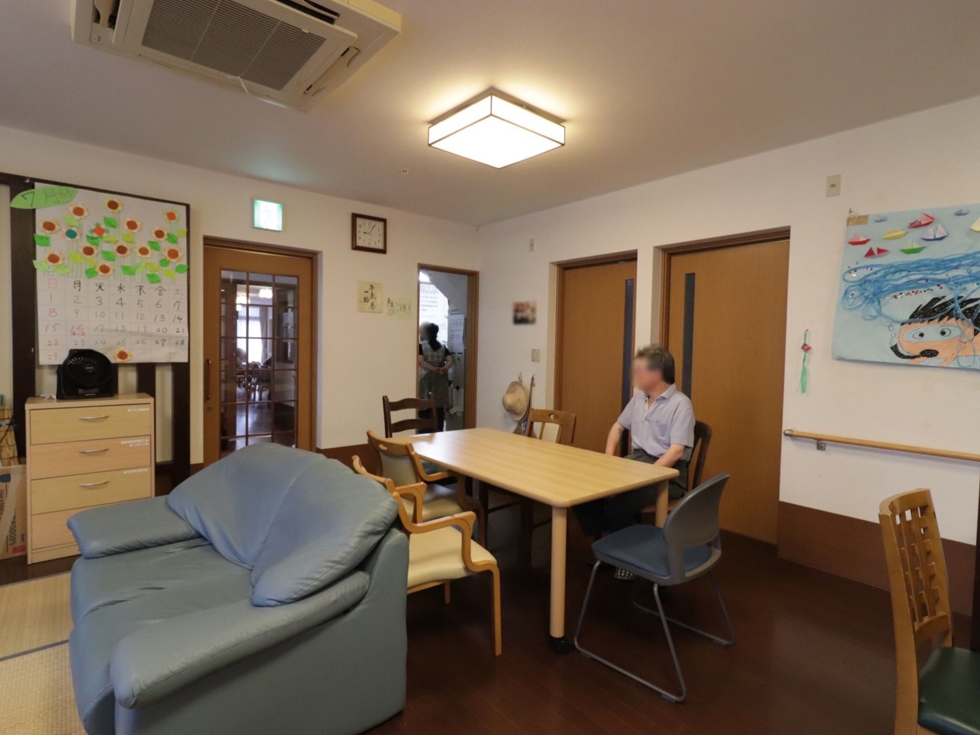 共有スペースに設置された椅子に入居者様が座り、のんびりくつろいでいる。天井に空調設備も完備されている。