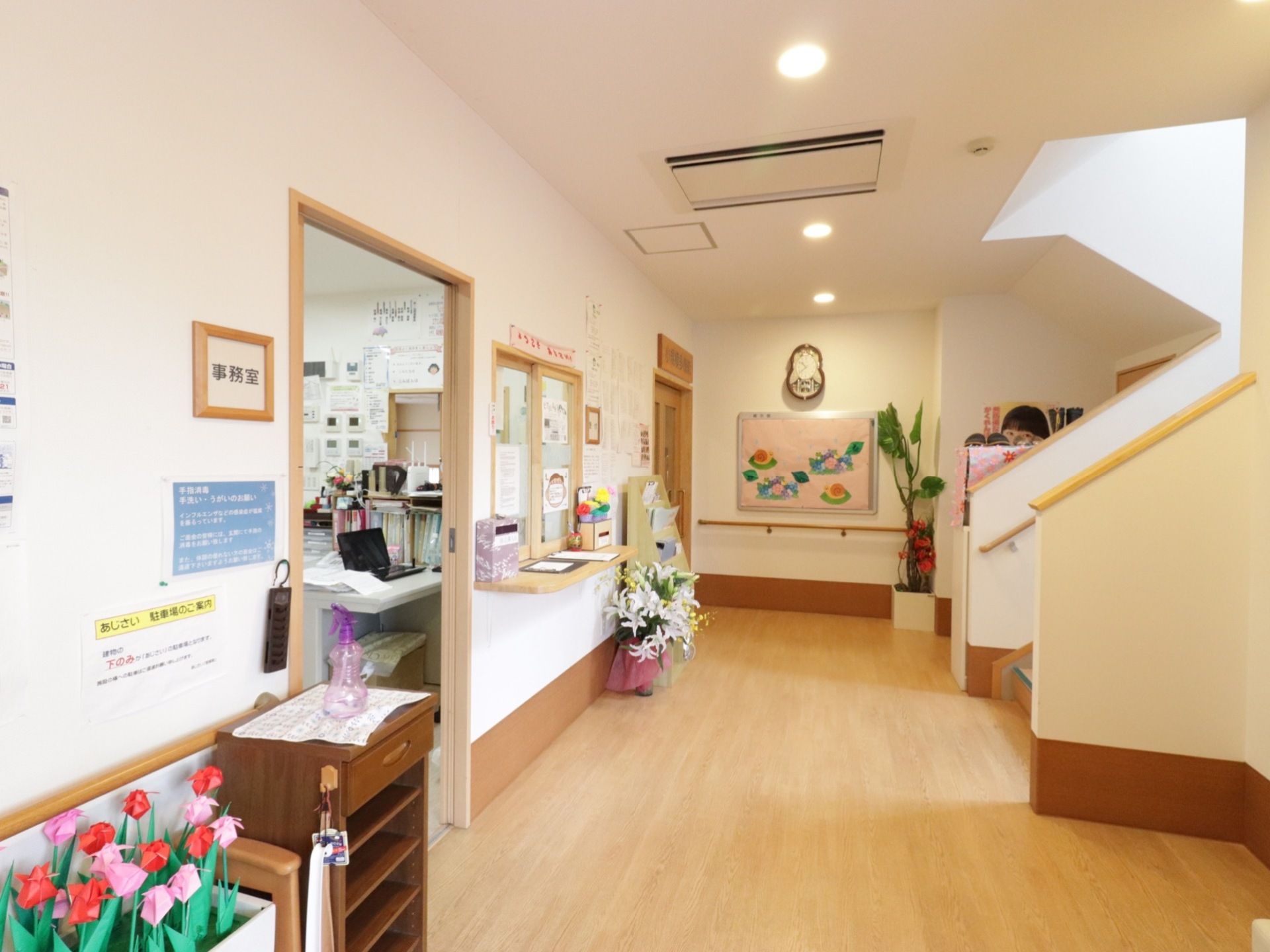 事務室には窓口があり、正面に階段が見えている。壁にはハンドメイドの飾りやお知らせのプリントが貼ってある。