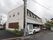 道路に面した場所に建つ、2階建ての施設である。電柱のとなりに白色の自動販売機、空き缶入れが設置されている。