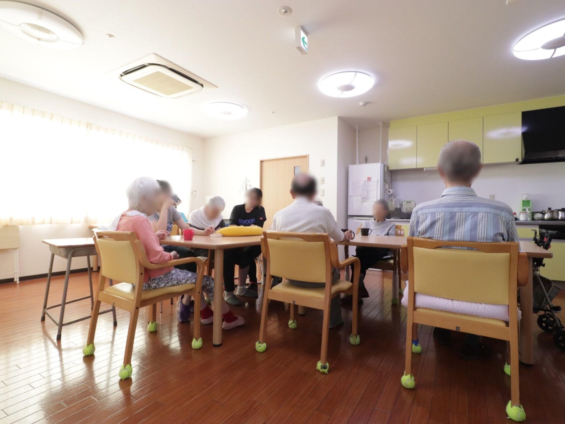 入居者様がテーブルを囲んでお茶を飲まれている。職員がエプロンを着用した入居者様のお手伝いを行っている。