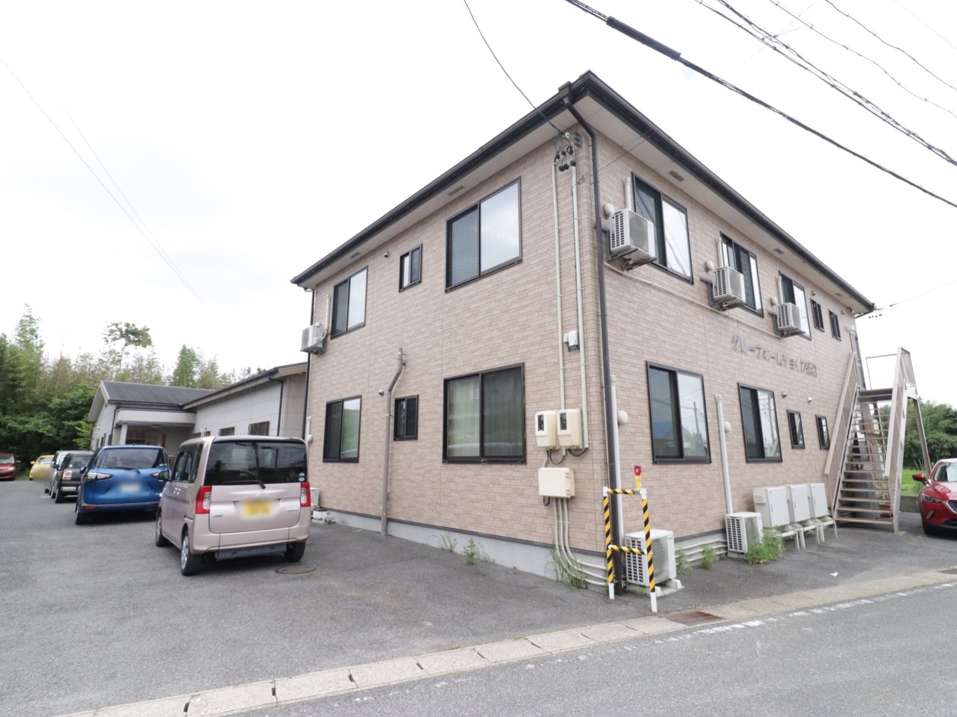 施設は、手前のコンパクトな２階建ての建物と奥側の平屋の建物が組み合わさった作りである。施設の手前には広々とした駐車スペースがある。