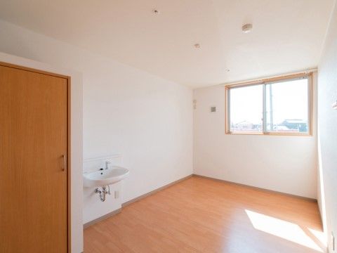 白い壁とナチュラル色のフローリングのシンプル空間である。窓から外の景色が見え、太陽の光が明るく室内を照らしている。