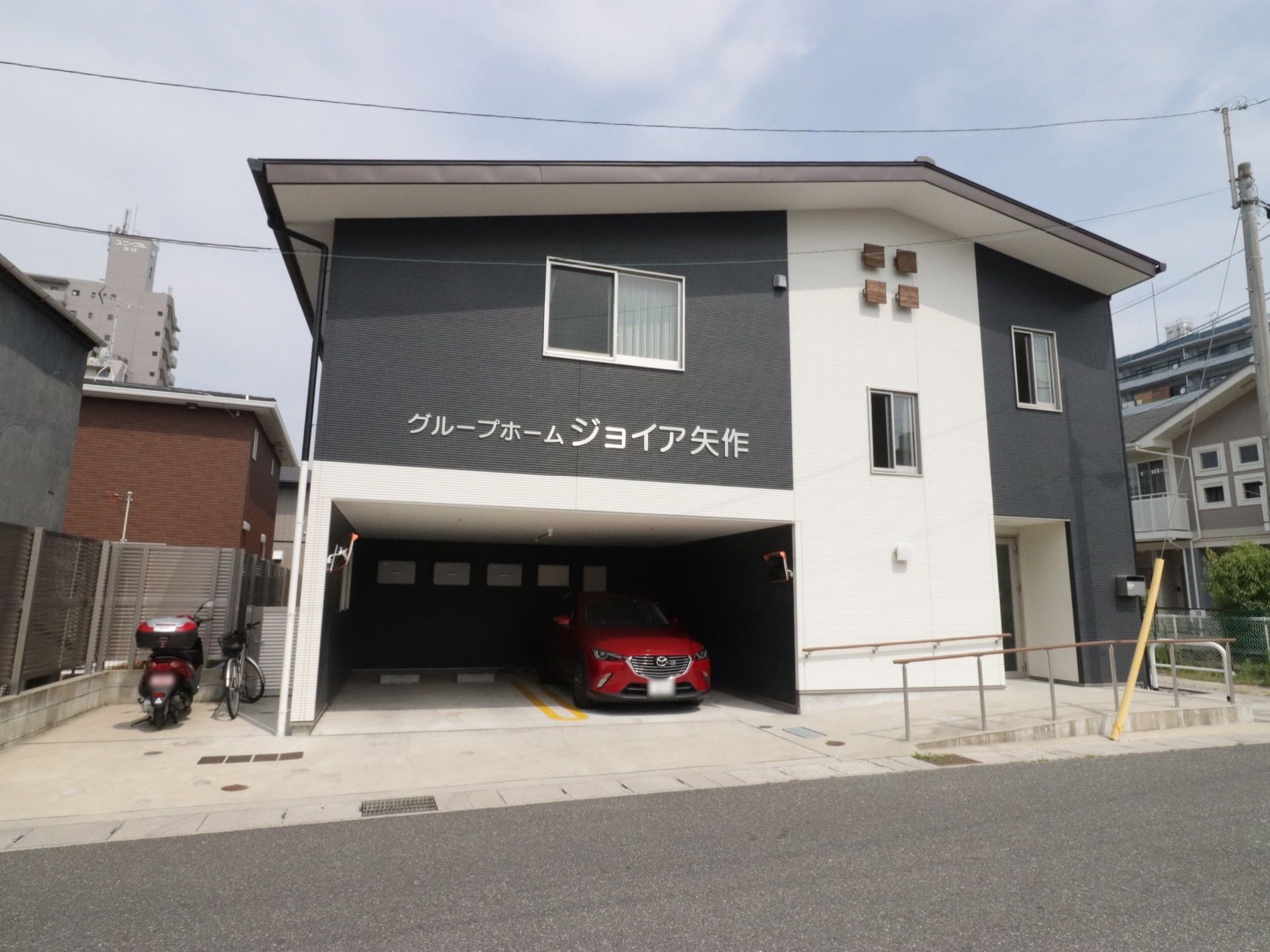 施設は、道路沿いに面したコンパクトな大きさの建物である。施設の敷地内には駐車場のほか駐輪場があり、建物の壁には施設の名称が表示されている。