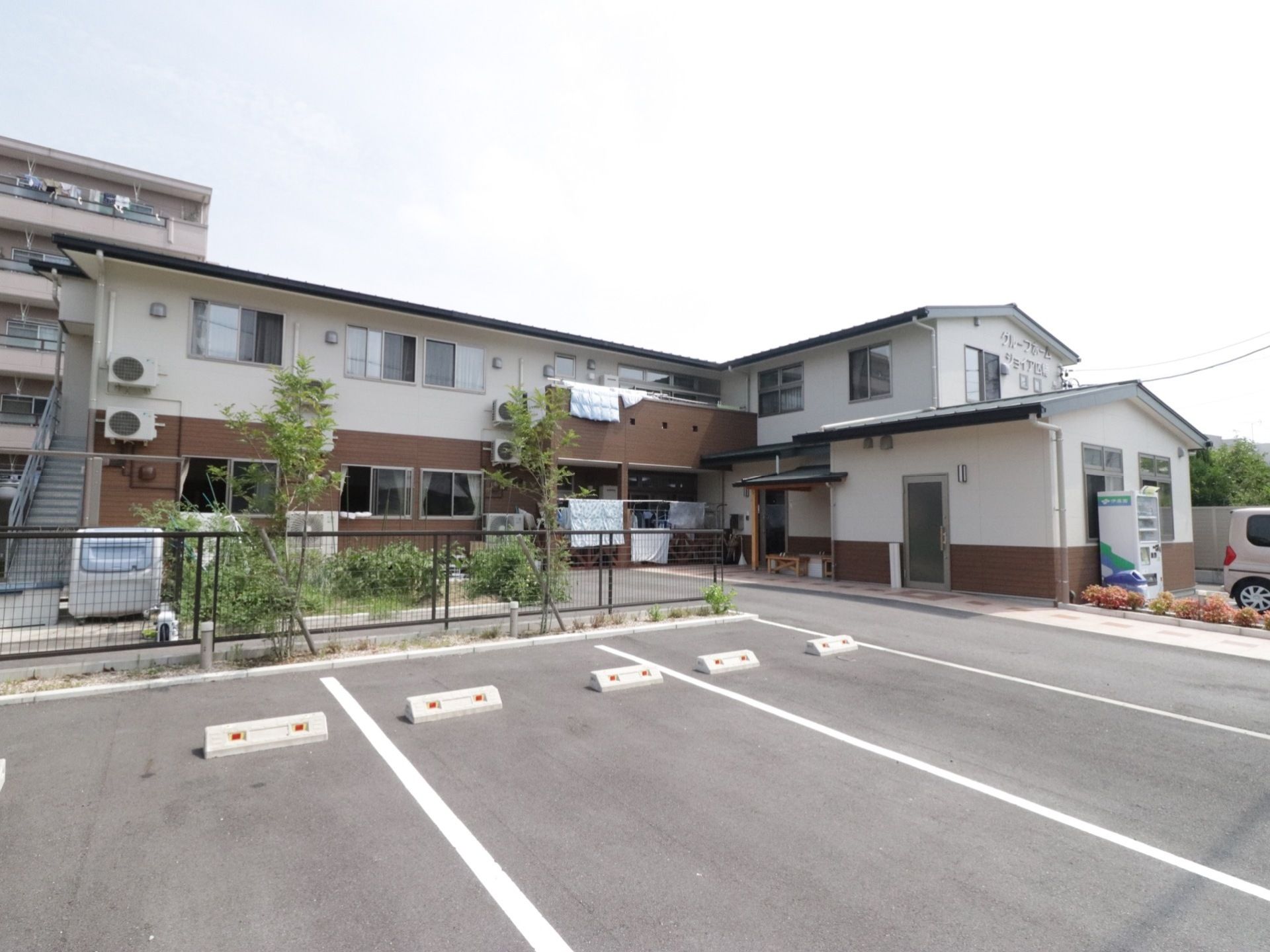施設は、白と茶色の壁が組み合わせられた、２階建てのコンパクトな建物である。ベランダには布団が干されており、のどかな光景が広がっている。