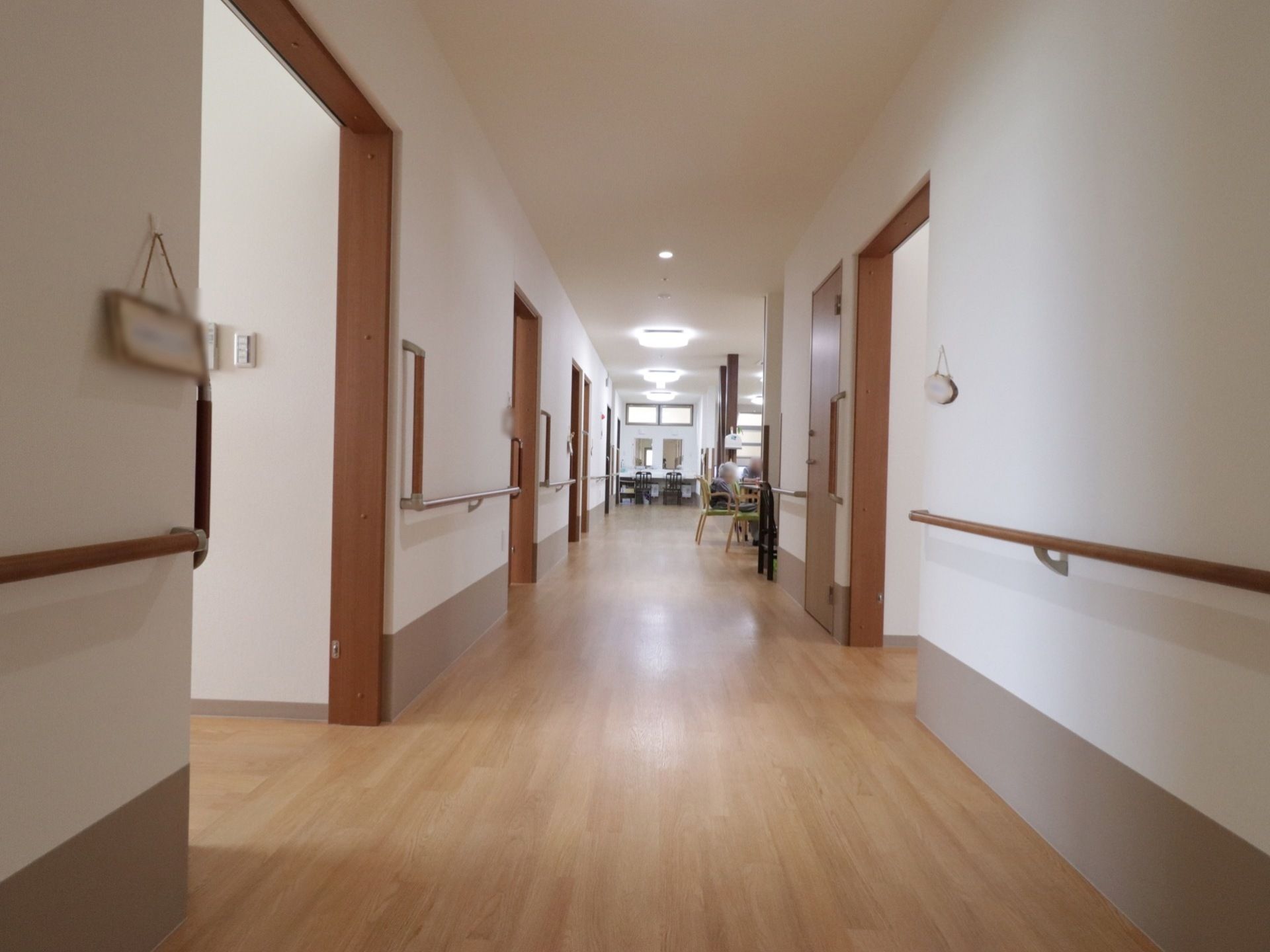 一直線上に続く廊下の壁の両側には入居者様の居室が並んでおり、各扉の隣には名札が吊り下げられている。居室の扉は非常に幅の広い設計である。