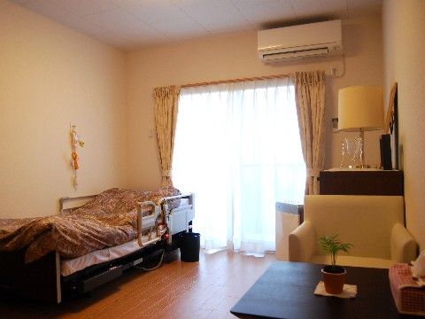 介護用のベッドとエアコンが設備されていて、１人掛けのこの字のソファーがある居住空間