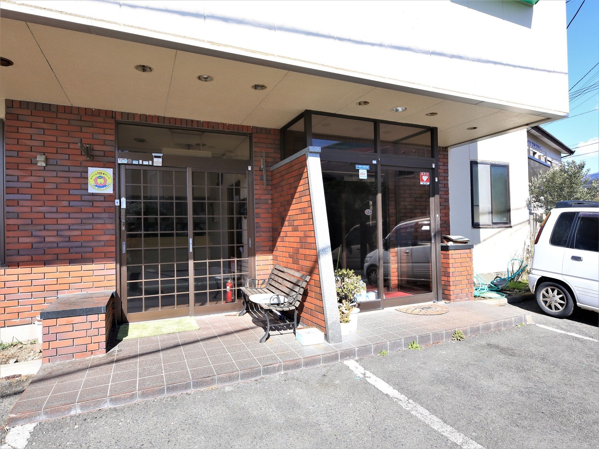施設内への入口が2ヶ所あり、左側の入口の前にはベンチが1台置かれている。入口前には駐車スペースが設けられている。