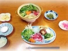 牛肉、椎茸、えのき、人参などが盛られた皿と、すき焼き鍋