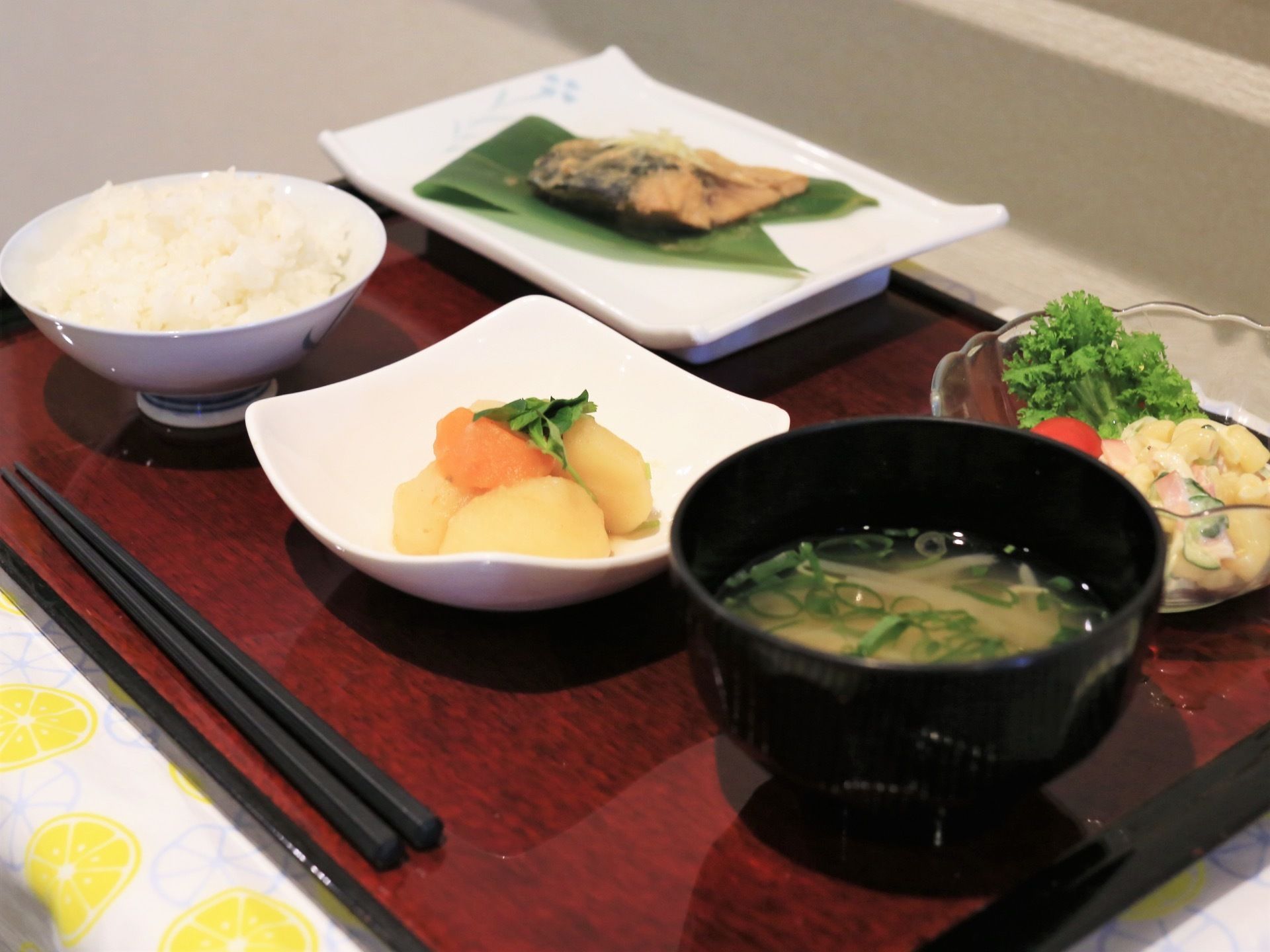 四角いトレーにご飯や味噌汁、煮物などが並べられている。お箸も添えられていて、食べやすい量になっている。