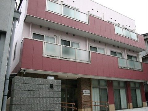 優しい色合いの外観の３階建ての施設である。玄関前には両側に手すりのついたスロープが設置されていてバリアフリーになっている。