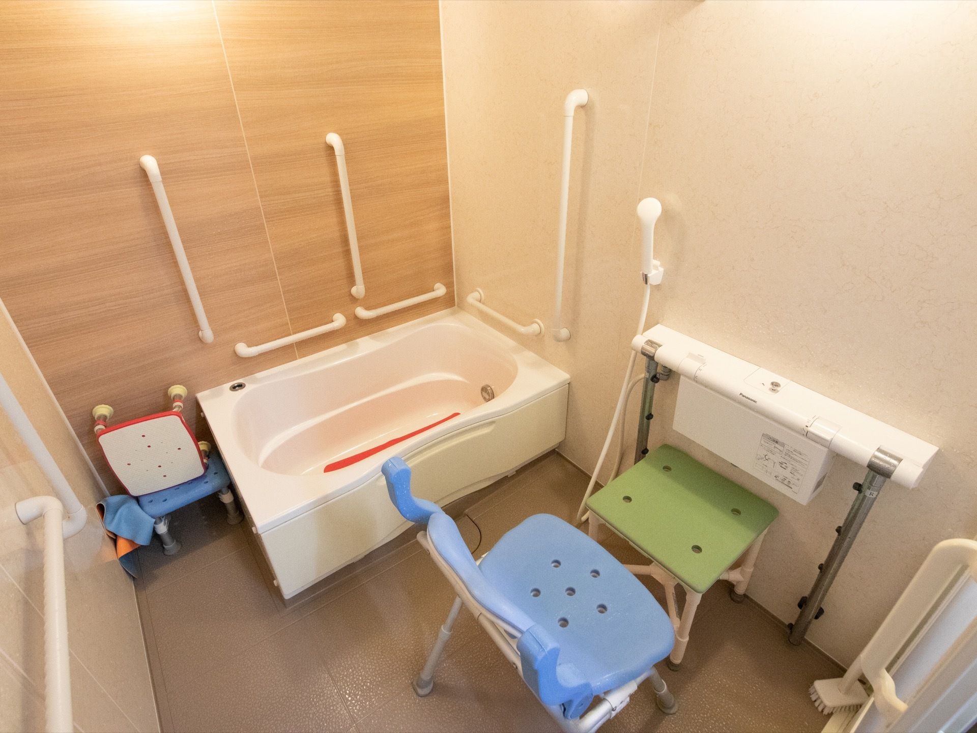 個人用の浴室。シャワーなど水道の操作は白いバー状の物で行う。浴槽回りには縦横の手すりが取りつけられている。