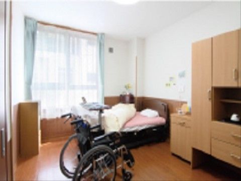 ワンルームの個室タイプの居室。フローリングの床で、窓にはレースとブルーのカーテンが取り付けられている。
