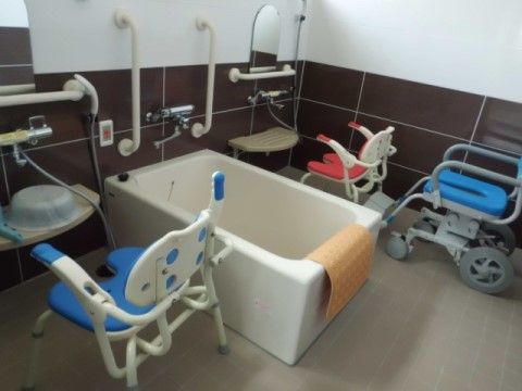 鏡が取り付けられた洗い場には、シャワーチェアや浴室用の車椅子が用意されている。壁には複数の手すりが設置されている。