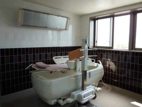 ゆとりあるバスタブが置かれた広々とした介護浴室である。下は黒色、上は白色を基調としたタイル張りの壁となっている。