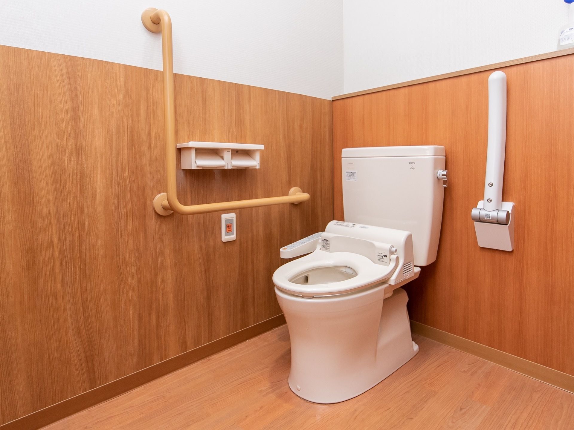 ゆったりとしたスペースに温水洗浄便座付きのトイレがあり、壁には手すりが設置されている。呼び出しボタンも取りつけられている。
