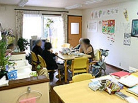 テーブルが２つ用意されており、窓際のテーブルに入居者様が座っている。片方のテーブルにはティッシュやファイルが置いてある。