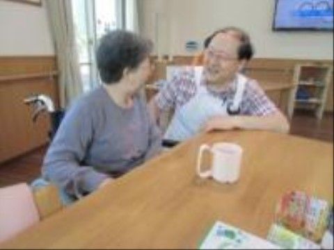 食堂で談笑する入居者様とスタッフ。入居者様の前には、取っ手が大きく持ちやすいタイプのマグカップが置かれている。