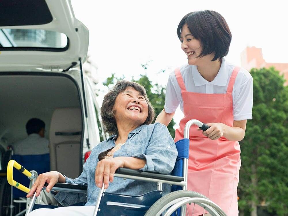 介護車両へ移動する車椅子に乗った高齢女性と介助をする女性ヘルパー