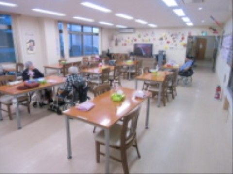 テーブルが余裕を持って並べられた共有スペースである。大型テレビが置かれており、入居者様が思い思いにくつろいでいる。