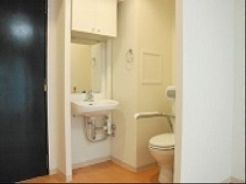 洗面台がついたトイレ。床には段差がなく、トイレには手すりを取り付けている。洗面台の上には収納棚がある。