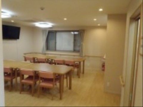 広い室内に数組のダイニングテーブルセットが置かれている。壁には手すりとテレビ、広い窓が設置されている。