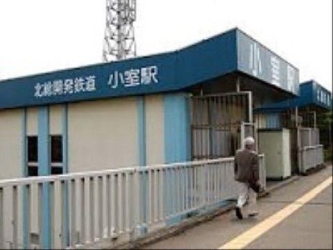 オフホワイトの外壁に、水色の柱と青い屋根が特徴的な駅の外観。屋根部分には白い文字で駅名と鉄道会社名が書かれている。