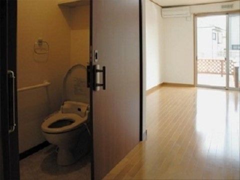 縦長の取っ手が付いた、開口部が大きな引き戸式の扉を開けると温水洗浄便座がある。壁には床と水平方向の手すりが付いている。