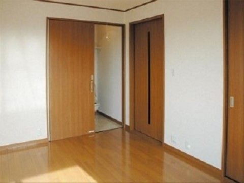 白い壁にフローリング張りの床で、背中側に窓がある。部屋にはトイレのほかにドアが２枚ある。トイレは洋式で棚が吊られている。