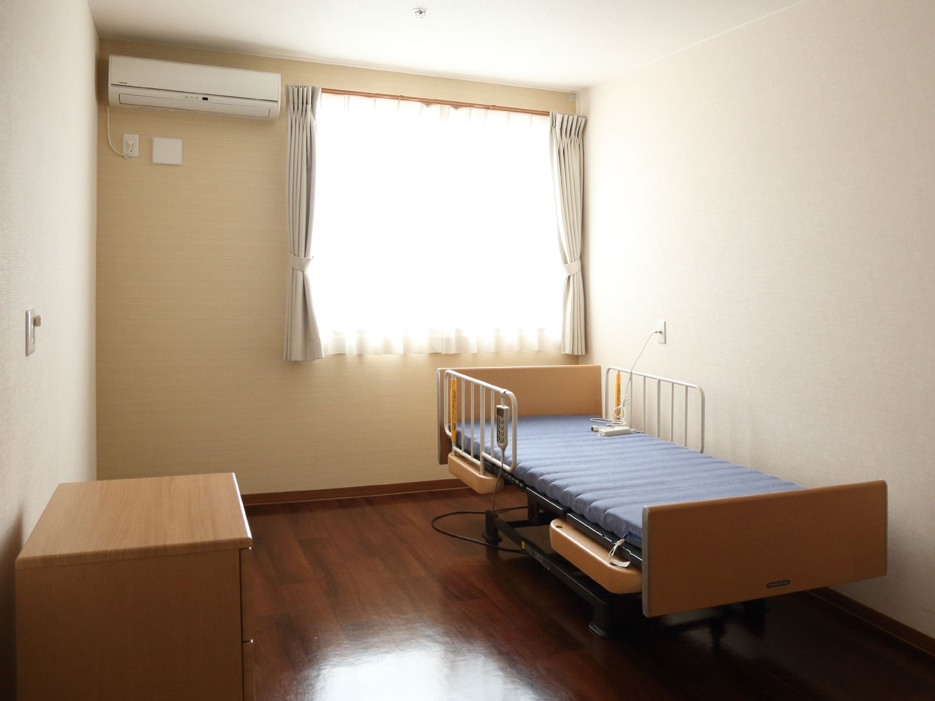 室内には、ベッドやチェスト、エアコンが据え付けられており、大きな窓があるため外からの光が差し込んでいる。