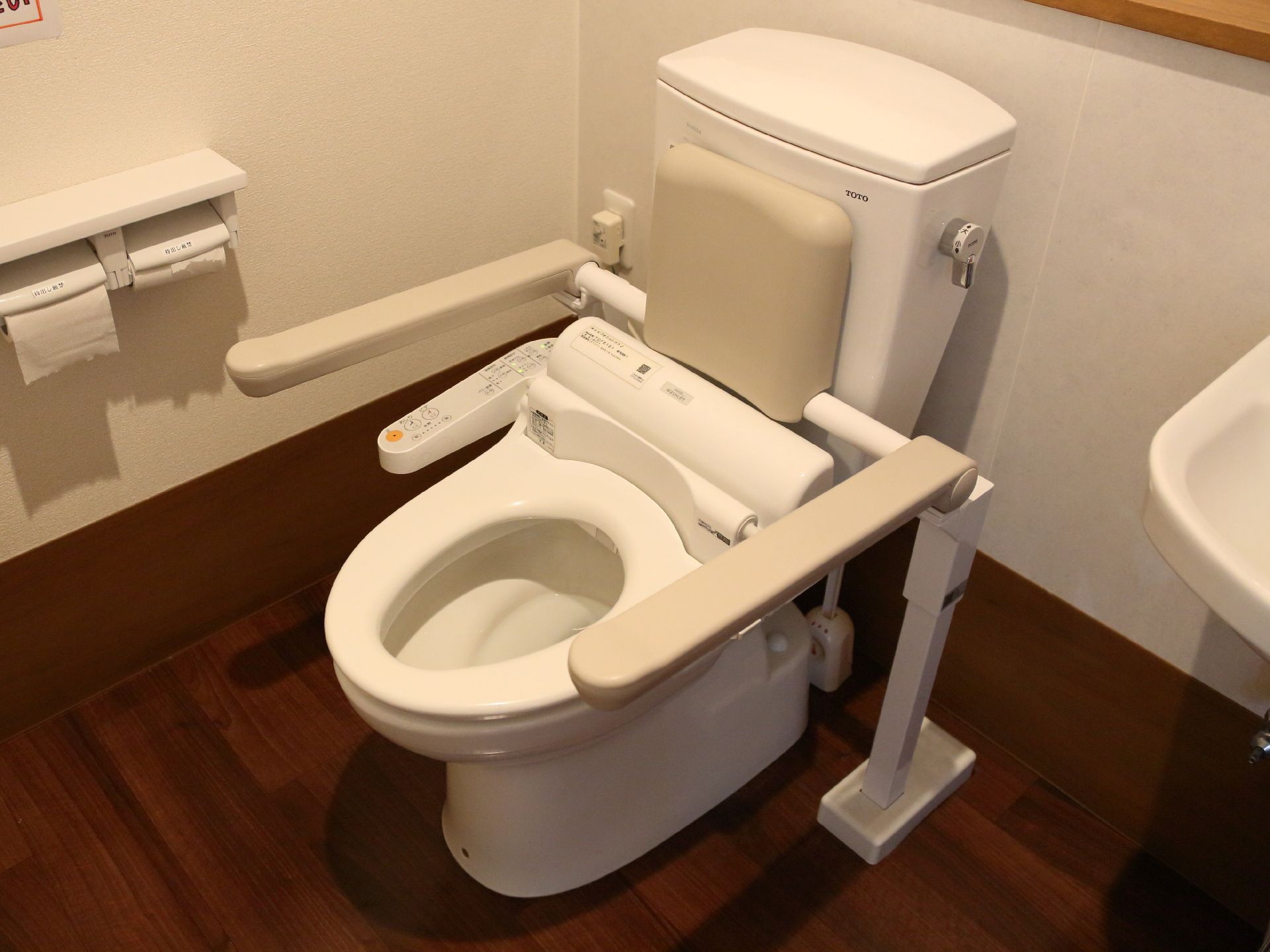 ウォシュレットがついたトイレには、両手で掴むことのできる手すりや背中当てパッドが設置されており、便器の周りにはスペースが広くとられている。
