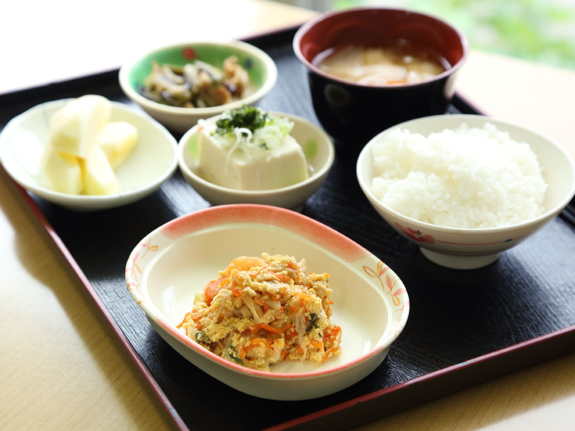 食事を１人ずつ黒色のトレーにのせて提供している。主菜や副菜、デザートも付いており、栄養バランスが考えられている。