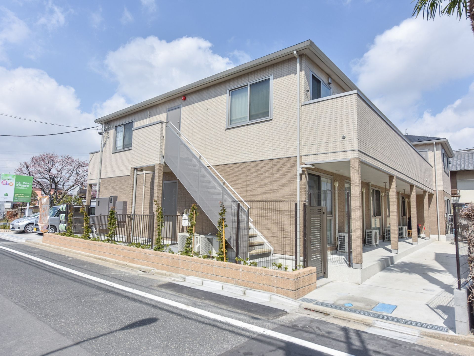 施設の外壁の2階からは非常階段がある。また、施設の側面からはすぐに道路がある。敷地内の地面は白に統一されている。