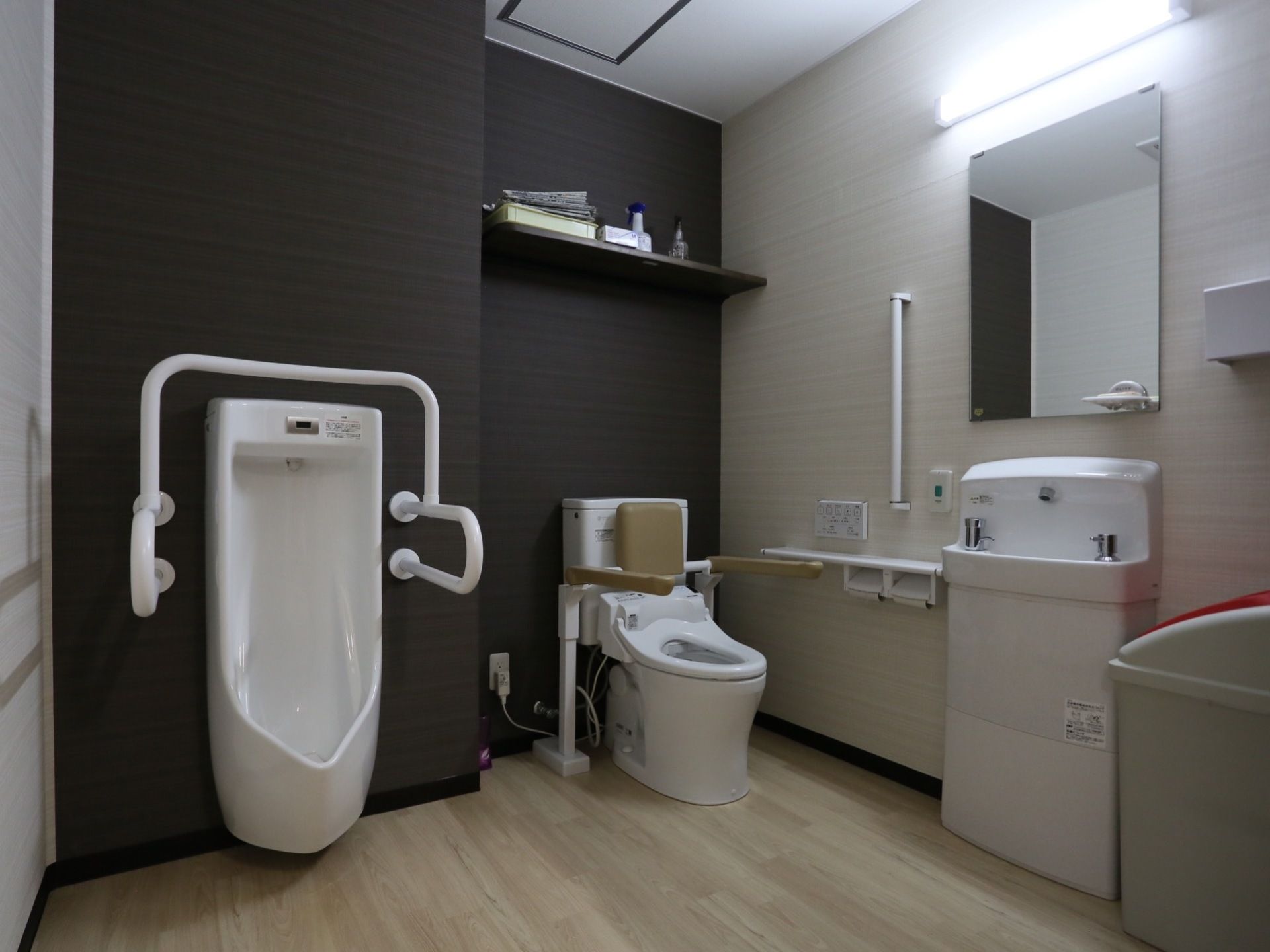 濃い色の壁紙が施された高級感のある落ち着いた空間に、洋式便器、小便器が据えられている。手洗器の上に大きな鏡が取りつけられている。