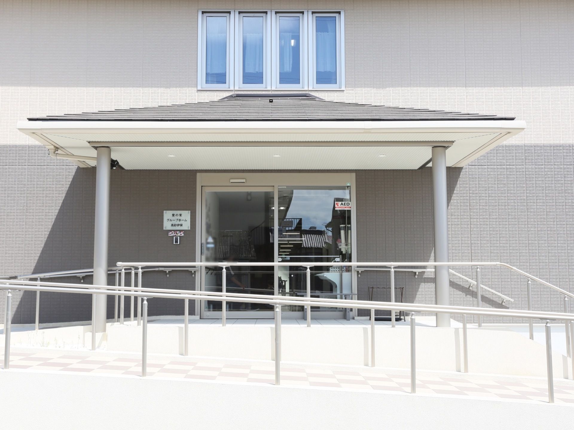 地面よりも高い位置にある自動ドアに向かって、ゆるやかな傾斜が折り返しながら続いている。自動ドアの前のスペースには大きな屋根が掛けられている。