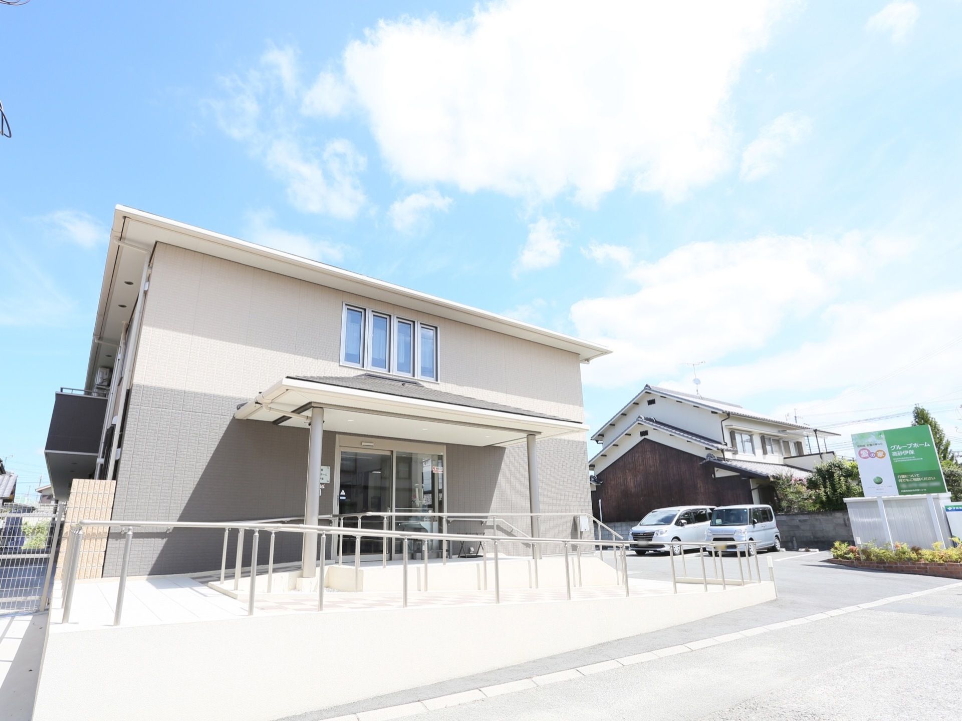 駐車場に隣接して２階建ての施設が建っている。玄関へのアプローチは、傾斜をゆるやかにするためにくの字に設計されている。