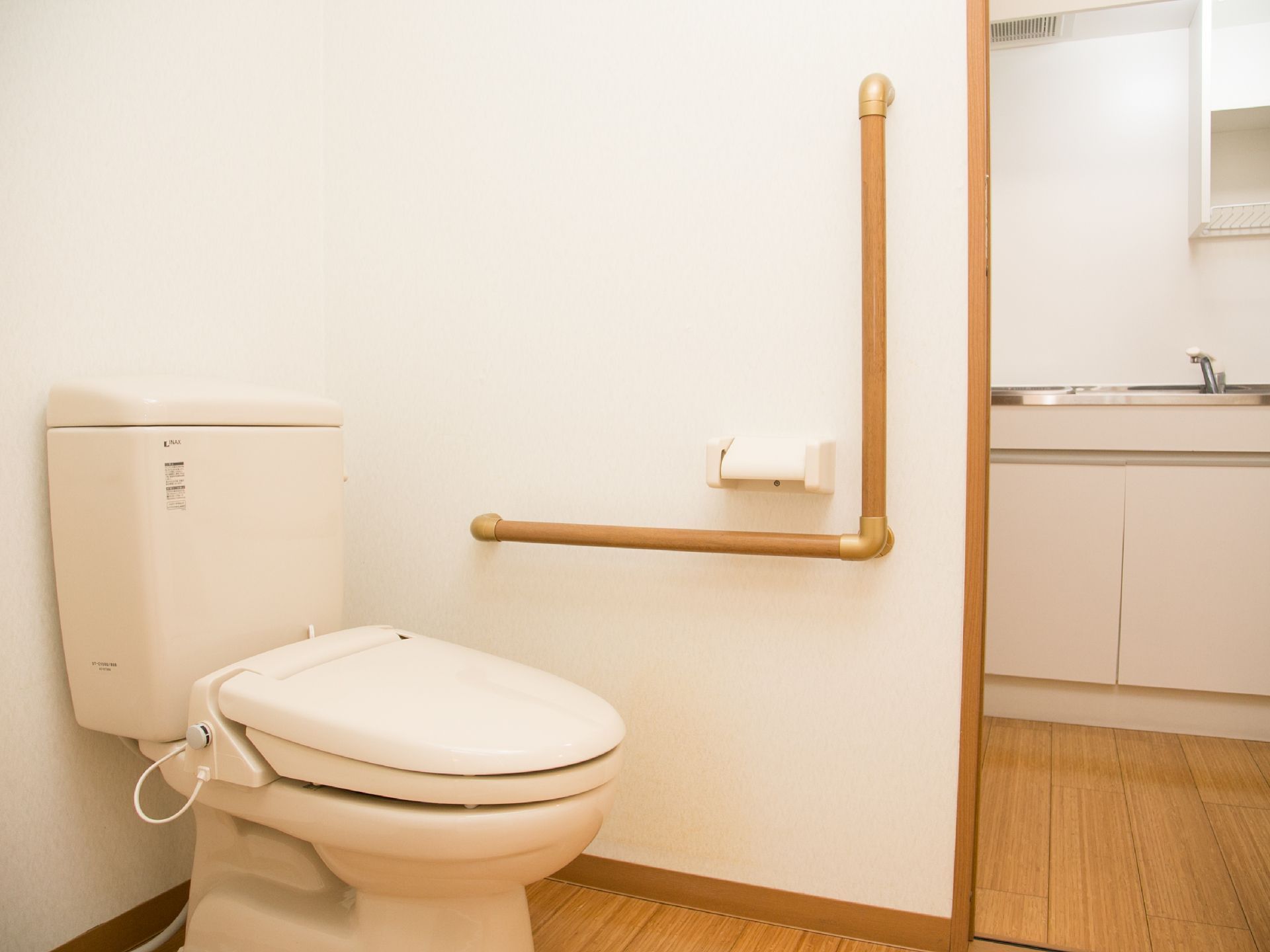 居室内のトイレの入り口には段差がないので、車椅子の方にもストレスなくご利用頂ける。壁にはL字型の手すりが設置されている。