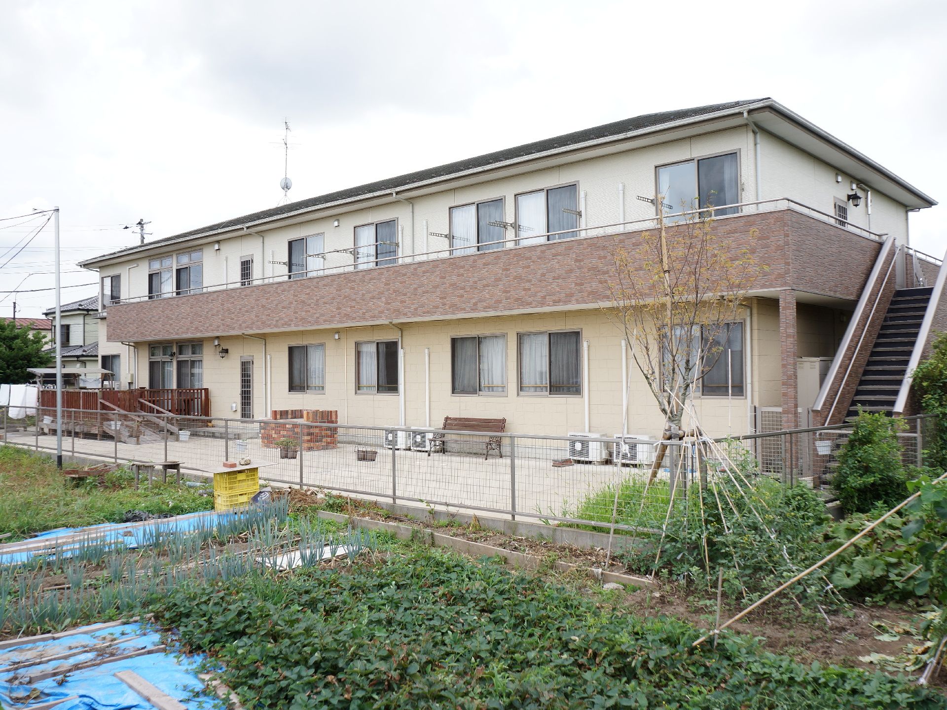 施設の隣には畑があり、緑が多い開放的な場所となっている。施設の横には階段があり、2階建てとなっている。