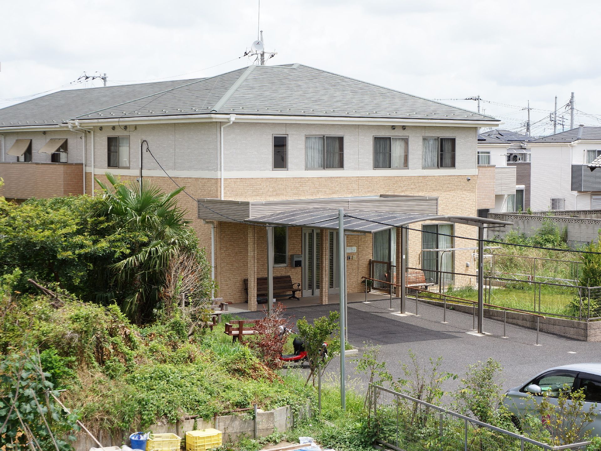 施設の前には車の入れる広めのスペースがあり、入り口までは屋根が設置されている。また、手すりやベンチも設置されている。
