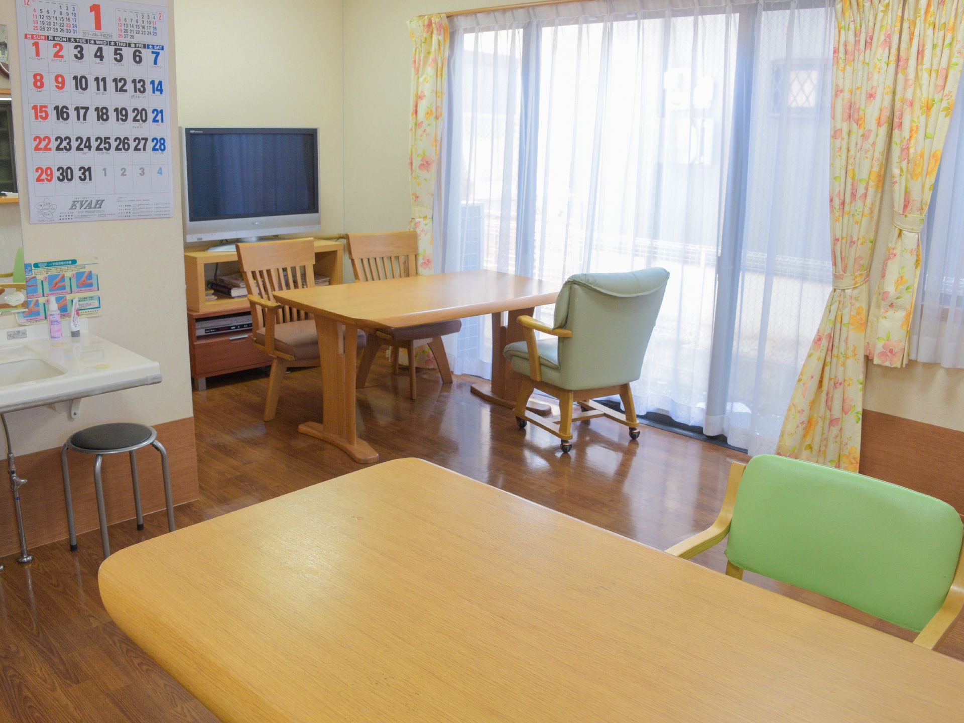 窓の大きい共有リビングは大変明るい雰囲気である。4人掛けの机と椅子が置かれている。談笑したりテレビを鑑賞したりと、好きな時間を過して頂ける。