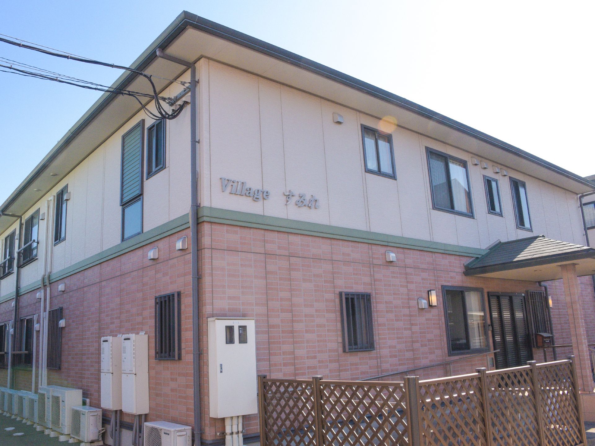 明るい色の建物の壁には、上方に施設名が書かれているので分かりやすい。窓がたくさん設けられている。玄関には照明が2つ付いている。